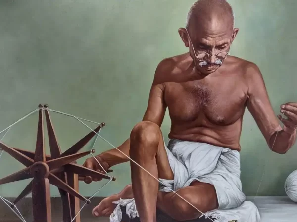 desenho do Maratma Gandhi sentado ao chão, vestindo apenas uma espécie de calção de pano de algodão branco, usando óculos de grau redondo e utilizando o tear.