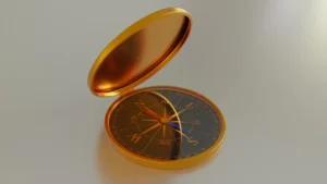Imaem de uma bússola de estrutura dourada, com fundo preto e ponteiros dourados, com a capa dourada aberta sobre um fundo branco acinzentado do que pode ser uma mesa.
