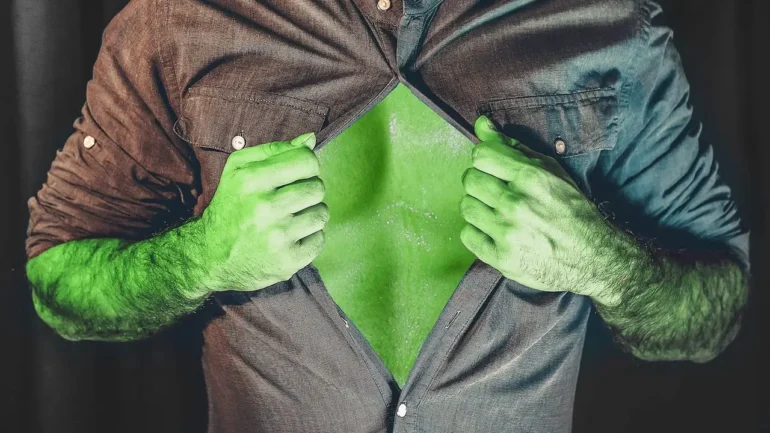Imagem do peito de um homem que está abrindo a camisa marrom, deixando aparecer o peito verde e forte.