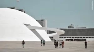 foto da Biblioteca Nacional de Brasília com algumas pessoas andando em direção a entrada principal, enquanto, se vê de longe, o vulto de outras aguardam na fila.