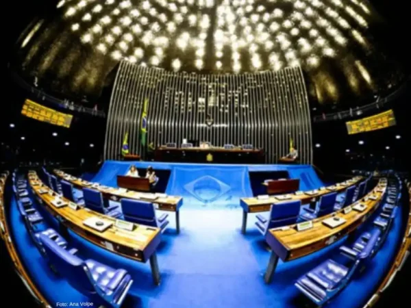 foto com a grande angular do plenário do Senado Federal em Brasília mostra as bancadas e poltronas da plenária e a mesa diretora a frente no palco. Ao centro no teto se destacam as luzes.
