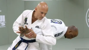 foto do lutador Royxe Gracie vestindo quimono e faixa preta em pé dando uma chave de braço em outro lutador também vestindo quimono de jiu-jitsu