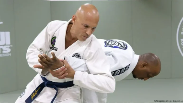 foto do lutador Royxe Gracie vestindo quimono e faixa preta em pé dando uma chave de braço em outro lutador também vestindo quimono de jiu-jitsu