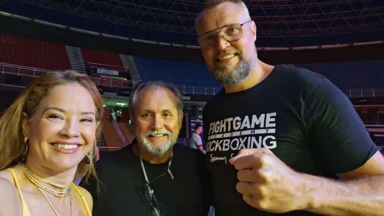 foto da tetracampeã de karate Carla Ribeiro, vestindo blusa de alça amarela e colar dourado, o Mestre Testa, vestindo uma blusa preta, e o tetracampeão do K1 Semmy Schilt, vestindo uma camiseta preta onde se lê FIGHT GAME - ACADEMY -KICKBOXING -SEMMY SCHILT.