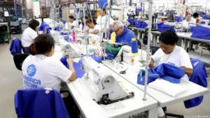 foto de uma fábrica de costura com várias mulheres com camisetas de uniforme costurando.