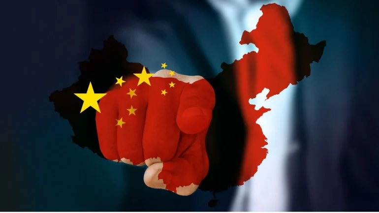 imagem da mão direita de um homem pintada com as cores vermelha e amarela da bandeira da China, vetindo terno e apontando o dedo indicador.