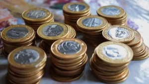 foto de várias pilhas de moedas de R$ 1,00 sobre um tampo de mesa de madeira.