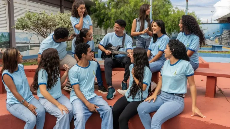 protocolo antirracista foto de 12 adolescentes estudantes no pátio da escola, vestindo uniformes, camisetas azuis claras e calças jeans, um deles está ao centro tocando violão. Sendo 9 meninas e 3 meninos.