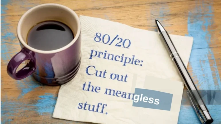 imagem de uma pequena caneca marrom com café, em cima de um bilhete escrito: 80/20 principle: Cut ou the meangless stuff. Em cima deste bilhete, uma caneta prata destampada. Tudo em cima de uma mesa de madeira clara.