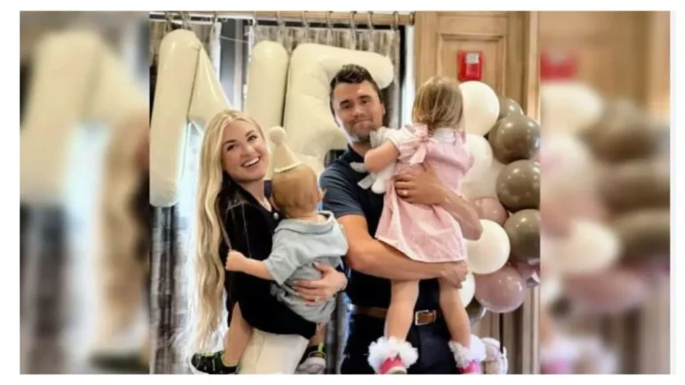 foto do conservador cristão CHARLIE KIRK com sua esposa. Ela carrega o filhinho e ele a filhinha. Ao fundo um salão com, balões e os 2 estão sorridentes.