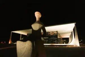 imagem da est&aacute;tua da justi&ccedil;a da Pra&ccedil;a dos 3 Poderes em Bras&iacute;lia, e ao fundo o STF, a noite.
