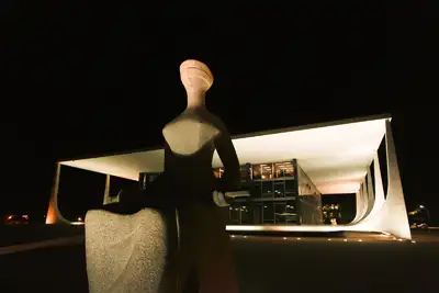 imagem da estátua da justiça da Praça dos 3 Poderes em Brasília, e ao fundo o STF, a noite.
